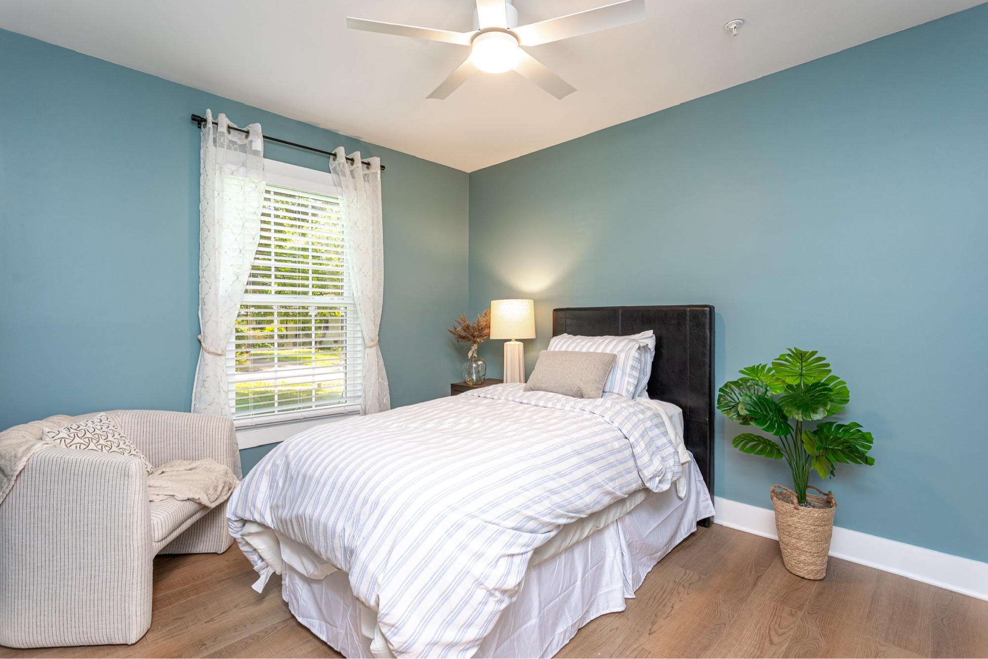 A bedroom with soft teal walls and light-wood floors
